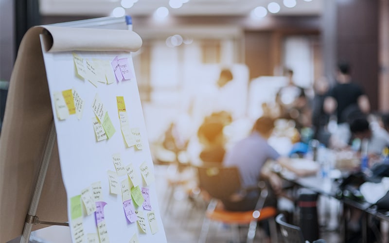 post-it notes on a board, employees at a table team building.